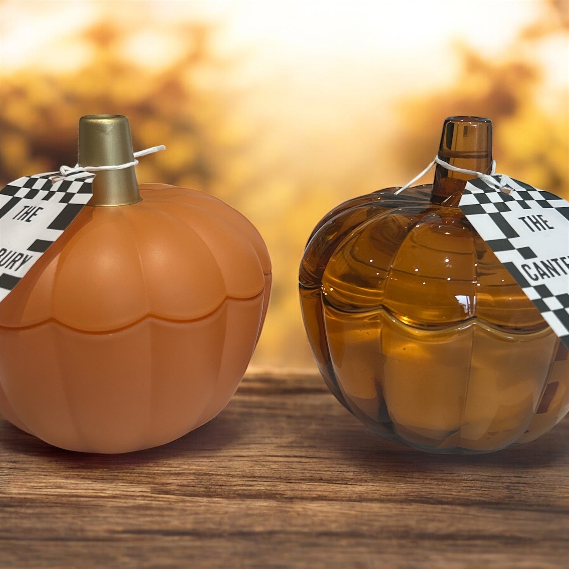 Two pumpkin-shaped bottles of perfume on a wooden surface with a blurred background.